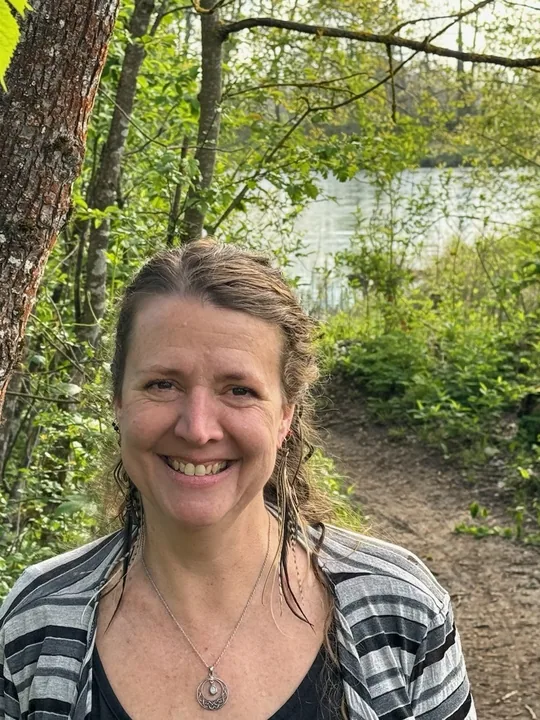 Becca Perry smiling on a wooded trail by the river